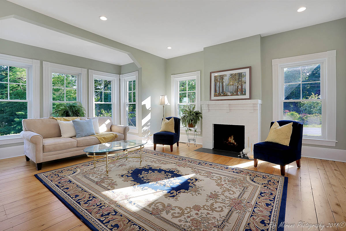 Renovated living room with bay window and brick fireplace in Boxford, MA by Next Level Builders